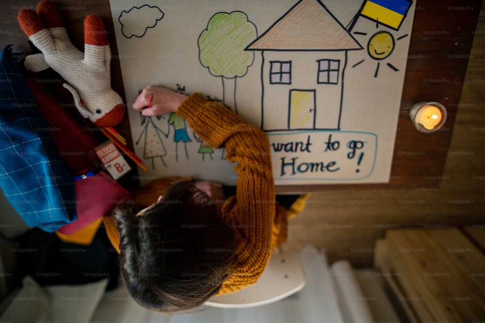 Eine Draufsicht auf eine ukrainische Flüchtlingsschülerin, die ihr Zuhause vermisst und ihre Familie zeichnet. Ukrainisches Kriegskonzept.