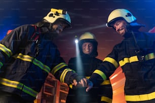 Glückliche Feuerwehrleute Männer und Frauen nach erfolgreichem Einsatz mit Feuerwehrauto im Hintergrund bei Nacht