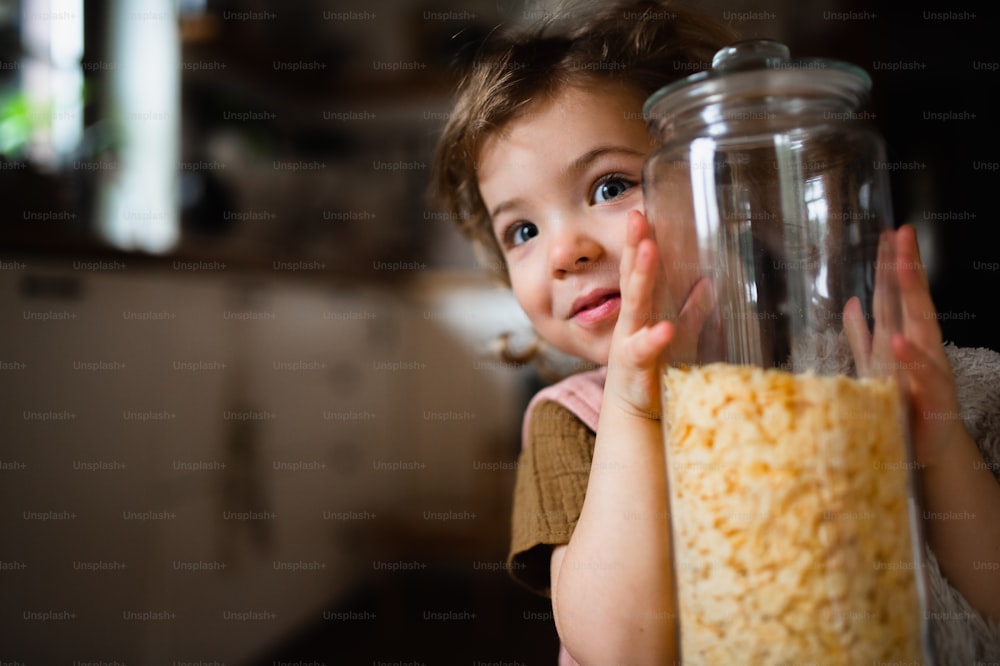 Ein Porträt eines niedlichen kleinen Behälters mit Cornflakes drinnen zu Hause, der in die Kamera schaut.