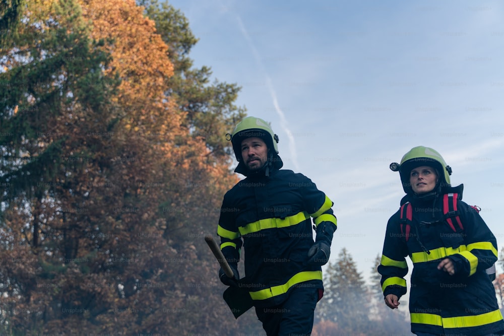 Bombeiros homem e mulher em uma ação, correndo através da fumaça com pás para parar o fogo na floresta.