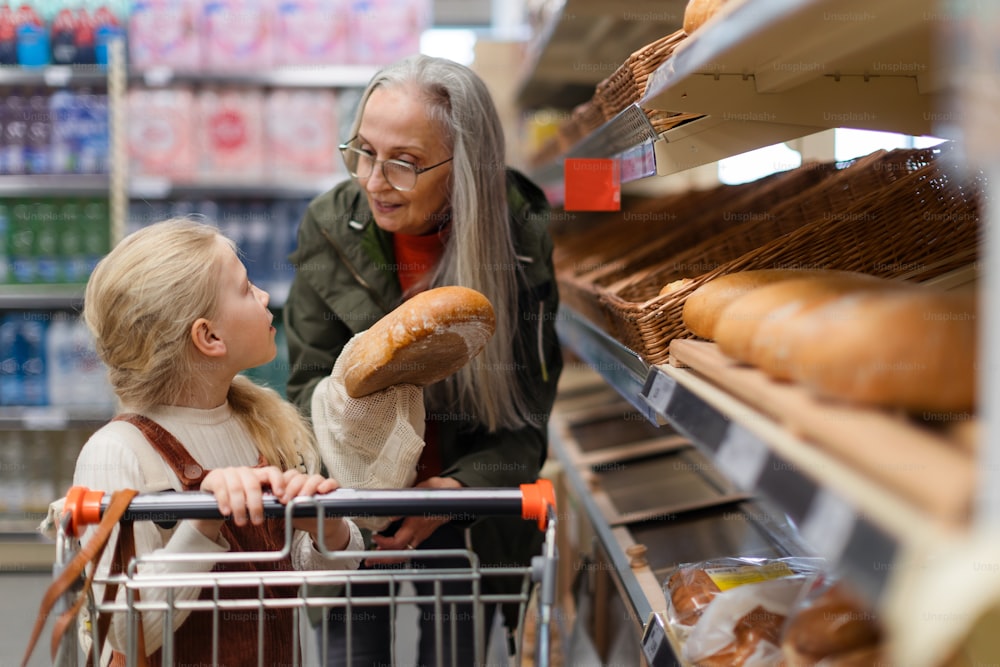 Avó com a neta escolhendo e comprando pão no supermercado.