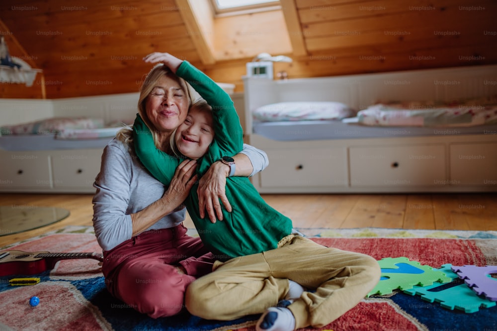 Um menino feliz com síndrome de Down sentado no chão e abraçado com sua avó em casa