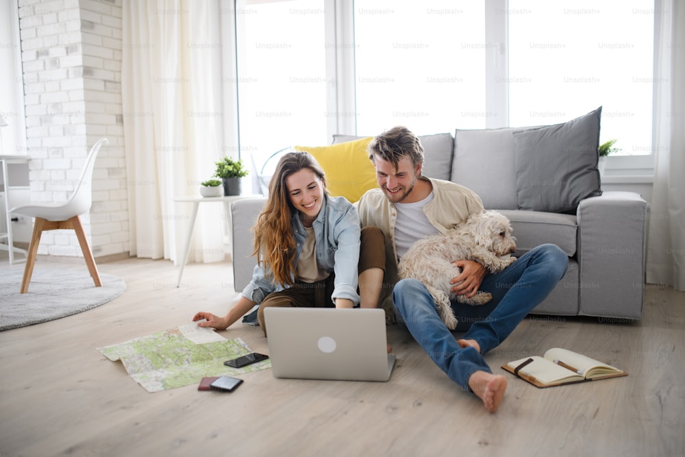 A happy young couple in love with dog planning holidays indoors at home, using laptop.