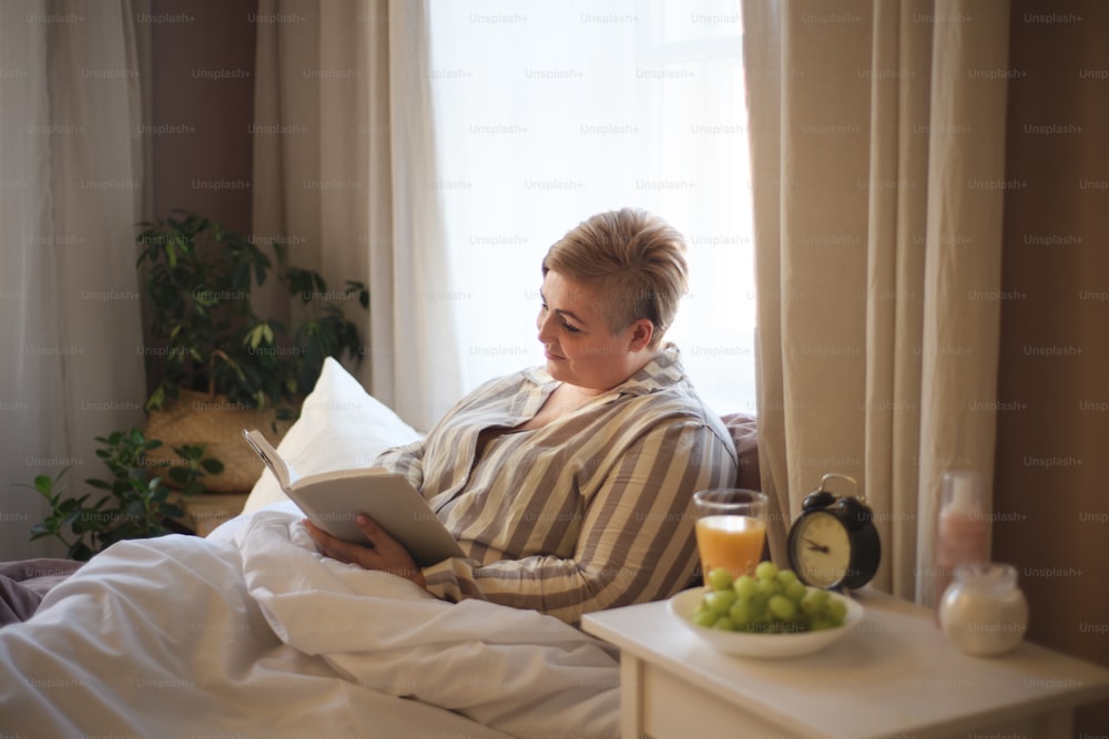 A happy overweight woman reading book in bed at home.