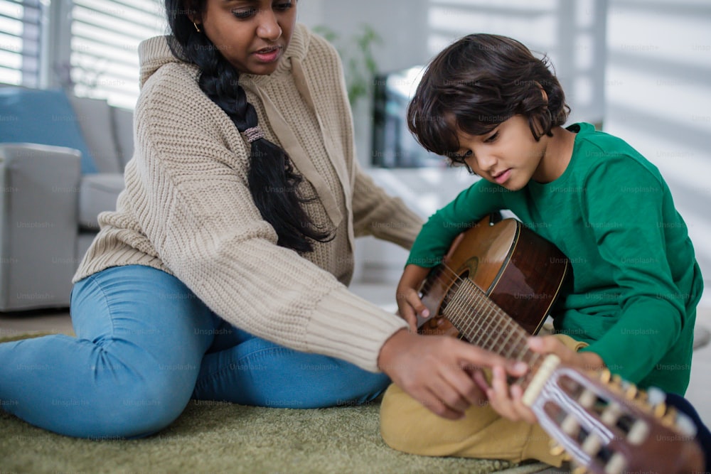 Un niño multirracial que aprende a tocar la guitarra con su madre en casa.