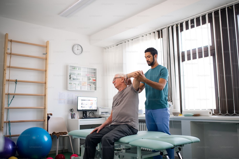Un jeune kinésithérapeute fait de l’exercice avec un patient âgé dans une salle de physique