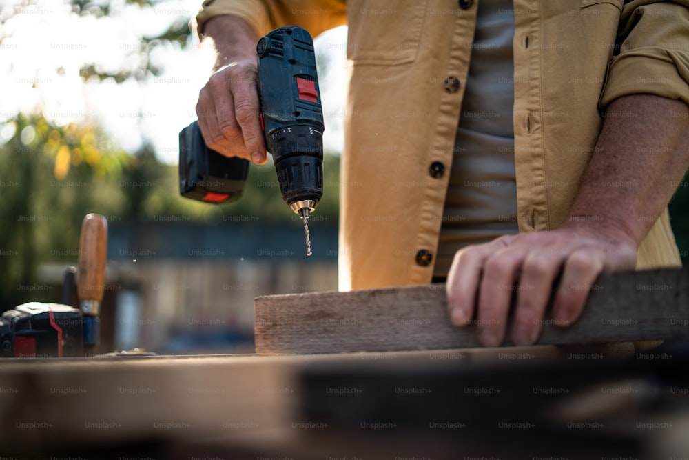 A close-up of handyman carpenter working in carpentry diy workshop outdoors with drill.