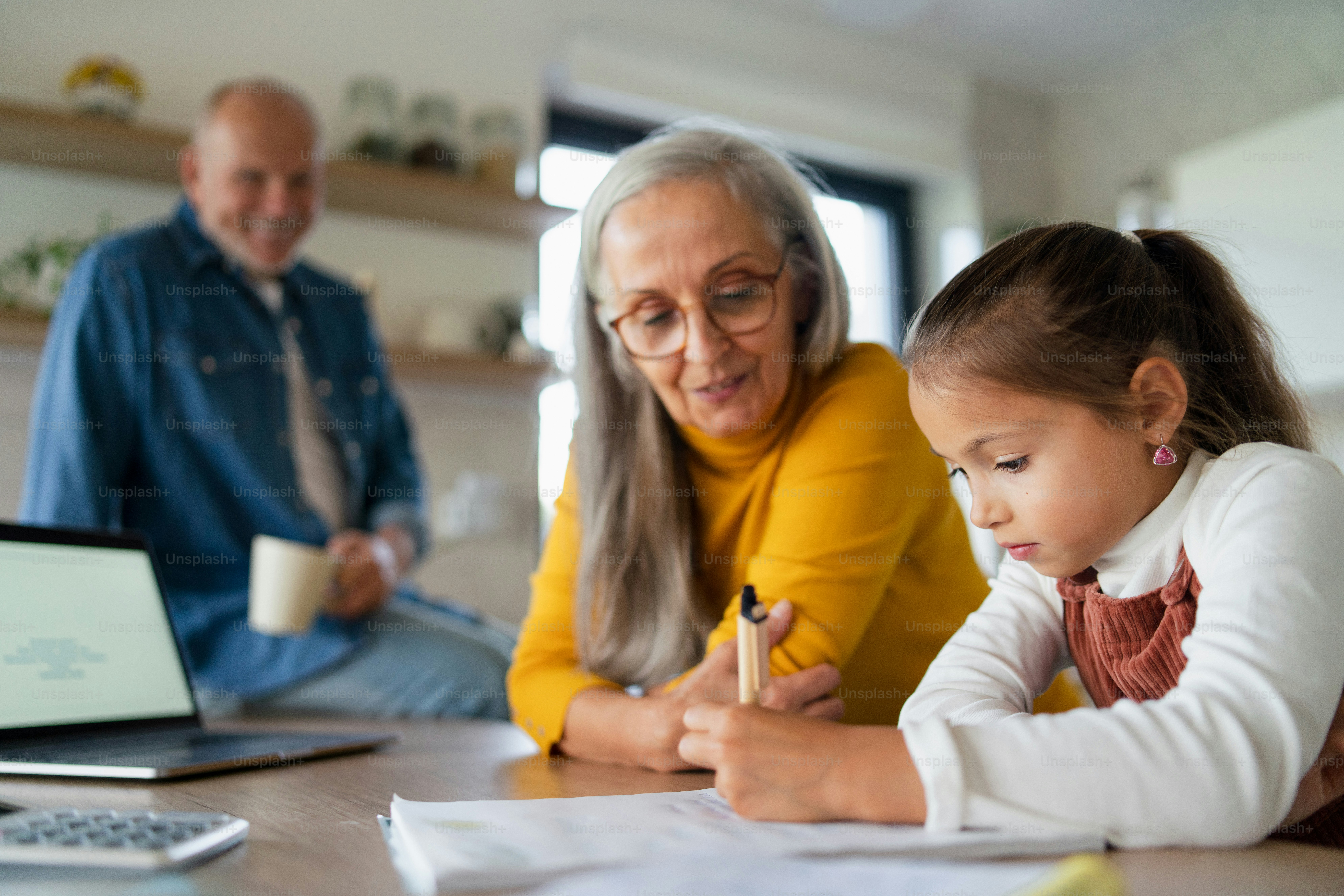 A small girl with senior grandparents doing maths homework at home ...