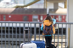 Eine Rückansicht eines ukrainischen Einwandererkindes mit Gepäck, das am Bahnhof wartet, ukrainisches Kriegskonzept.