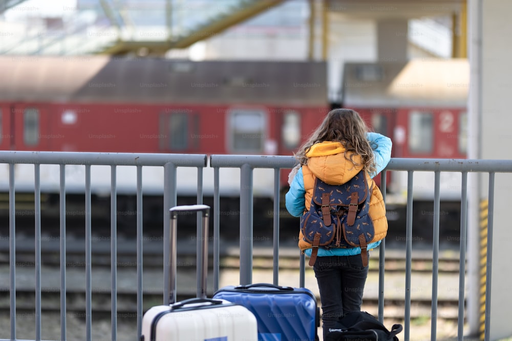 Vue arrière d’un enfant immigré ukrainien avec des bagages en attente à la gare, concept de guerre ukrainienne.