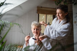 Une mère âgée heureuse en peignoir avec sa fille adulte à l’intérieur à la maison, concept de soins personnels.