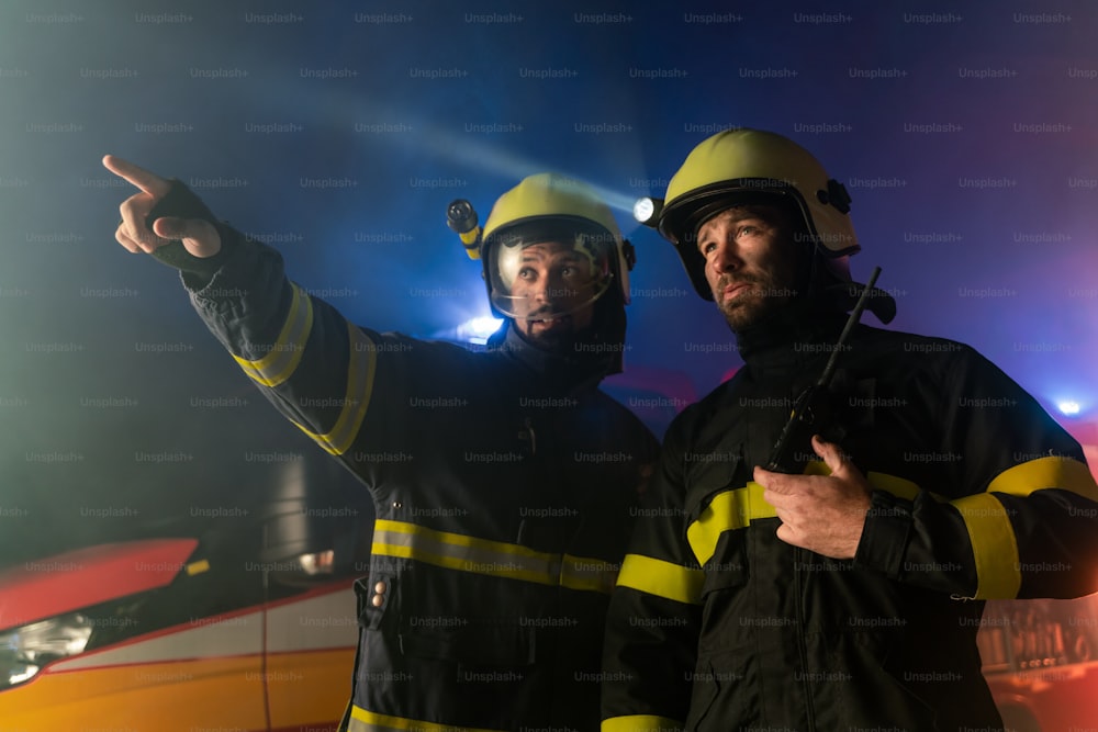 Uomini dei vigili del fuoco in azione con camion dei pompieri sullo sfondo in una notte
