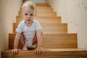 A cute little boy sitting on stairs at home and looking at camera.
