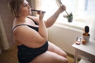 집에서 거울을 보고 앉아 있는 뚱뚱한 여자, 자기 관리 개념.