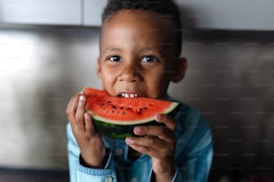 Garçon multiracial mangeant un melon dans la cuisine pendant les chaudes journées ensoleillées.