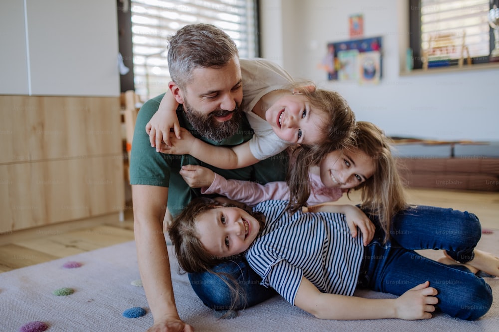 Ein fröhlicher Vater mit drei kleinen Töchtern, die zu Hause zusammen spielen.