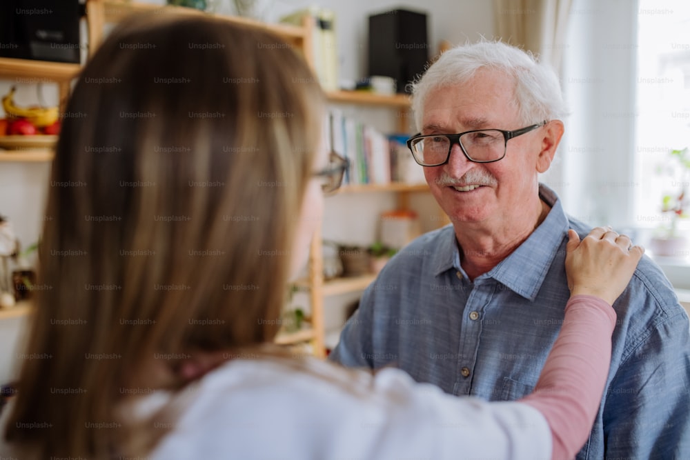 A healthcare worker or caregiver visiting senior man indoors at home.