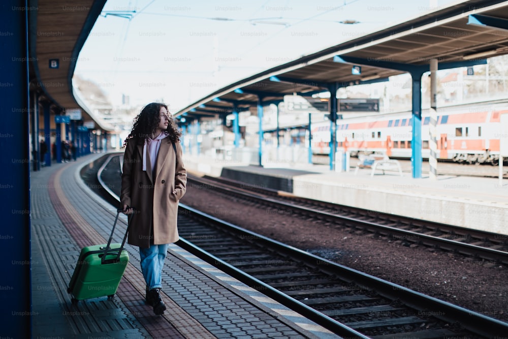 Uma mulher jovem viajante feliz com bagagem esperando por trem na plataforma da estação de trem