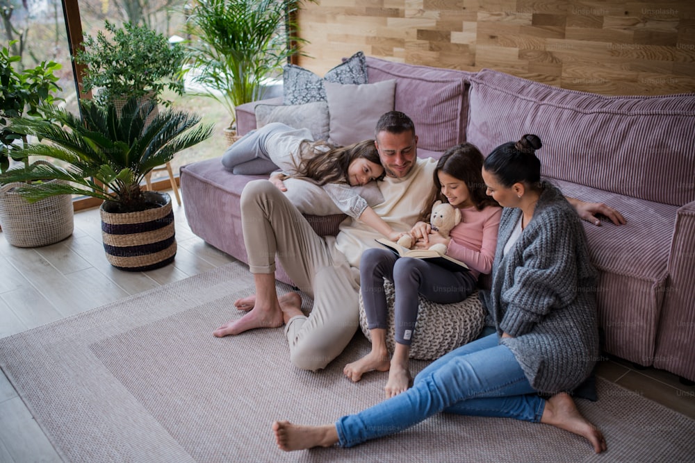Two happy sisters with a mother and father sitting on floor hugging and reading book at home