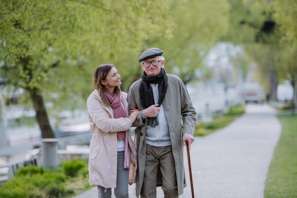 Un uomo anziano felice con bastone da passeggio e figlia adulta all'aperto durante una passeggiata nel parco.