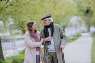 Un homme âgé heureux avec une canne et une fille adulte à l’extérieur lors d’une promenade dans un parc.