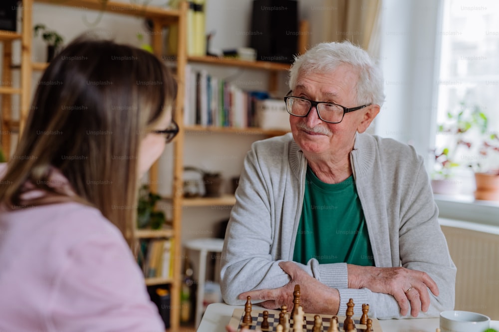 Eine erwachsene Tochter, die ihren älteren Vater zu Hause besucht und gemeinsam Schach spielt.