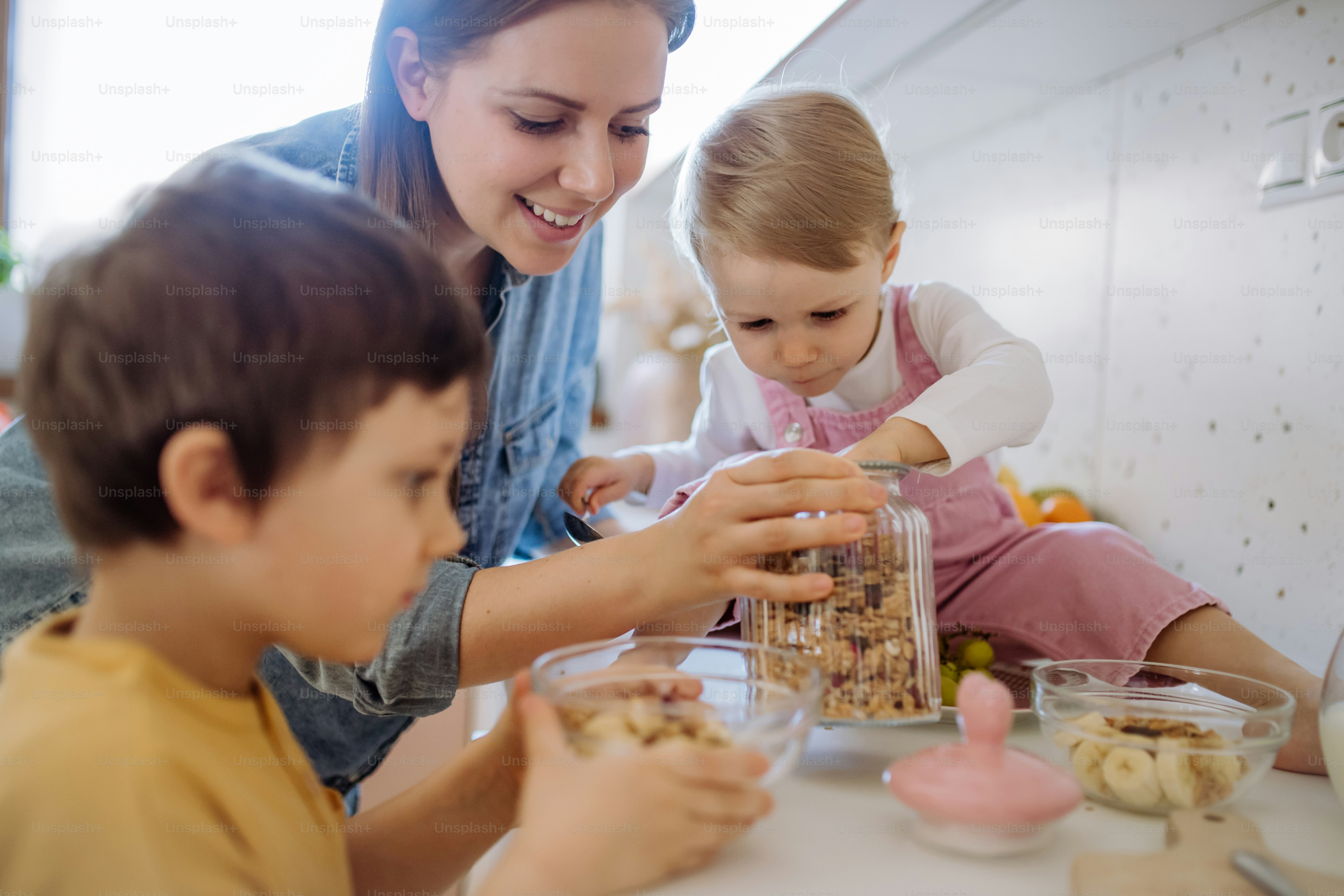 A mother of two little children preparing breakfast in kitchen at home ...
