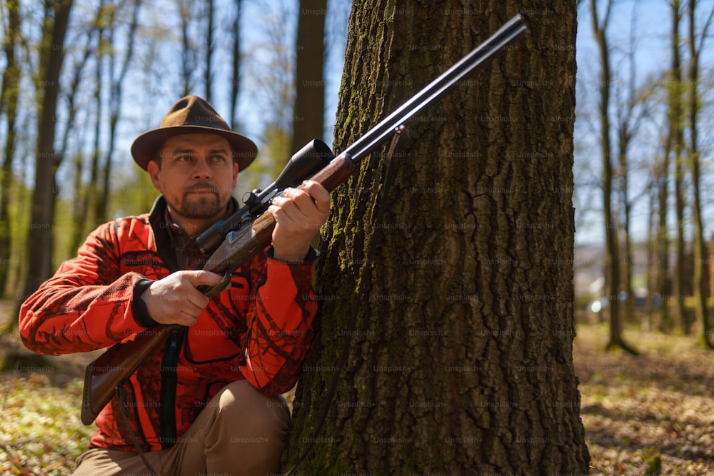 森の中で獲物を待つライフル銃を持ったハンターの男。