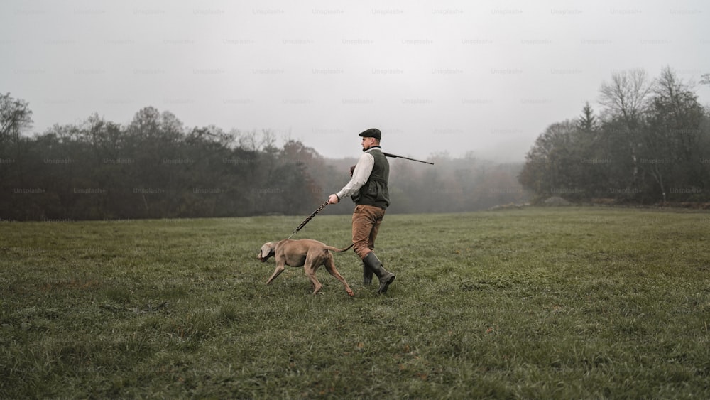 A hunter man with dog in traditional shooting clothes on field holding shotgun.