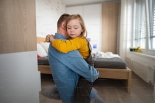 Ein Vater umarmt seine kleine Tochter mit Down-Syndrom zu Hause.