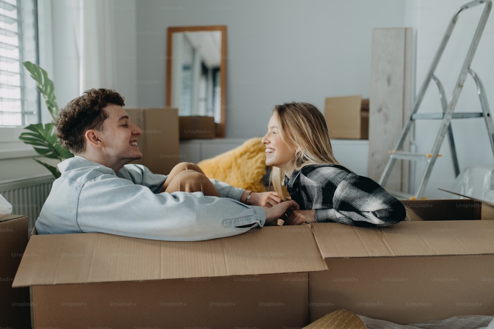 Una pareja joven y alegre en su nuevo apartamento, sentados en cajas y divirtiéndose. Concepción de la mudanza.