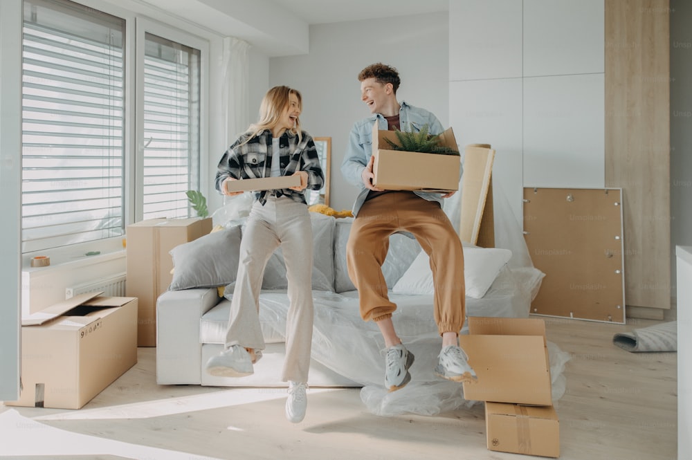 A cheerful young couple in their new apartment, carrying boxes. Conception of moving.