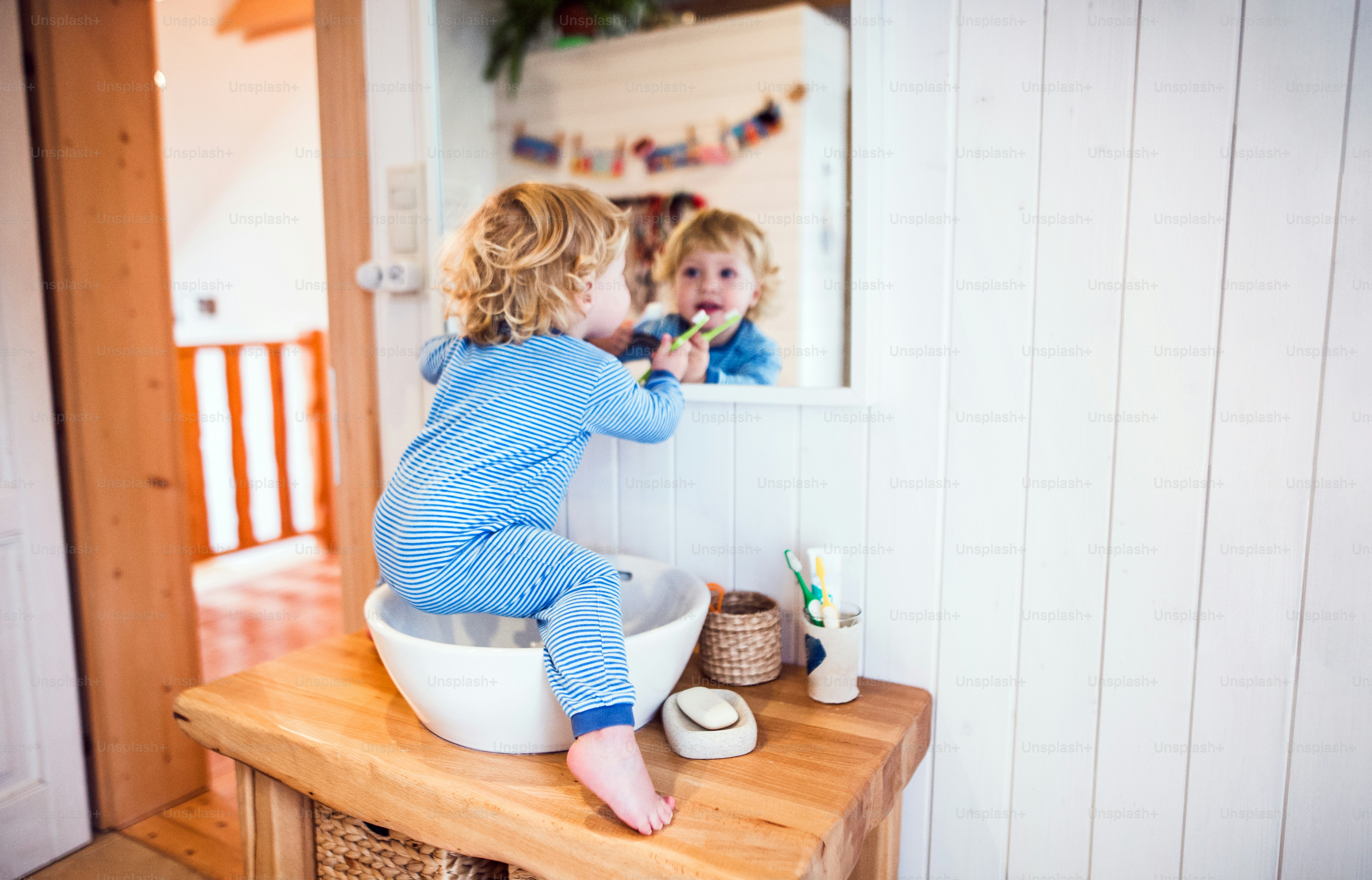Süßes Kleinkind, das sich im Badezimmer die Zähne putzt. Kleiner Junge sitzt auf einem Waschbecken. Hausunfall. Gefährliche Situation