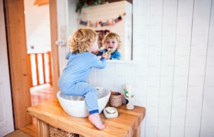 Süßes Kleinkind, das sich im Badezimmer die Zähne putzt. Kleiner Junge sitzt auf einem Waschbecken. Hausunfall. Gefährliche Situation.