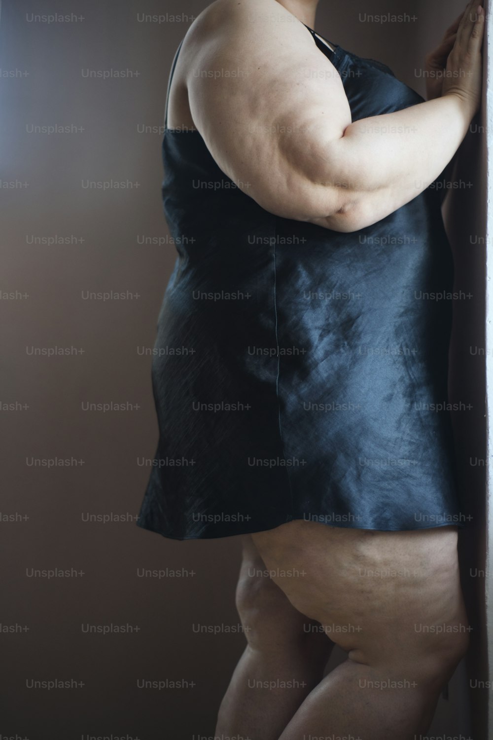 A midsection of lonely fat woman standing and looking through the window at home.