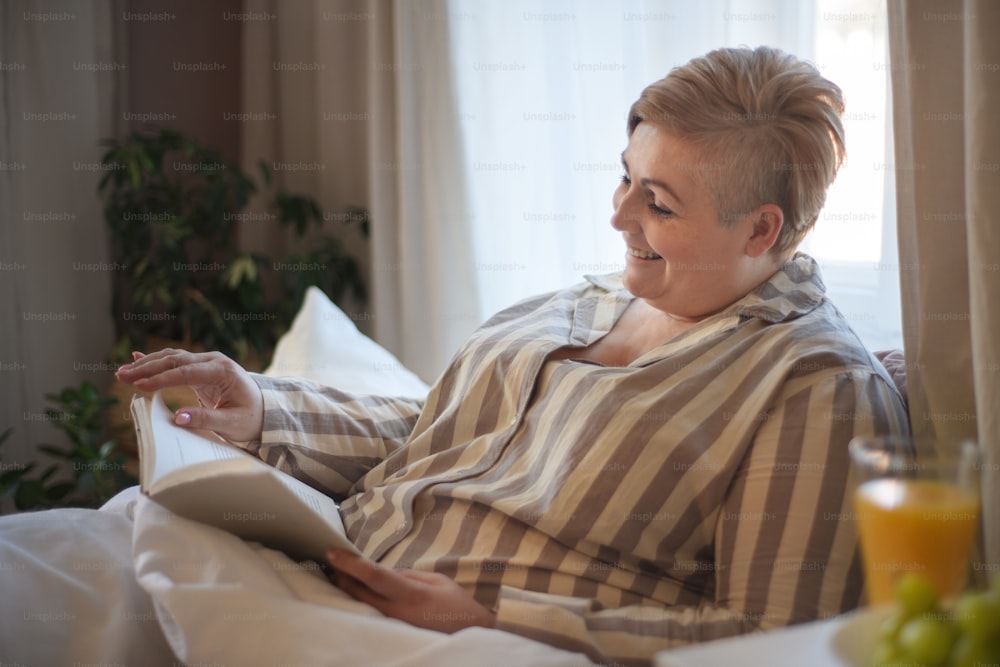 A happy overweight woman reading book in bed at home.