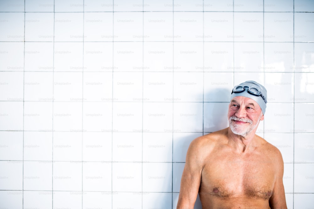 Portrait of a senior man standing against white background in an indoor swimming pool.. Active pensioner enjoying sport.