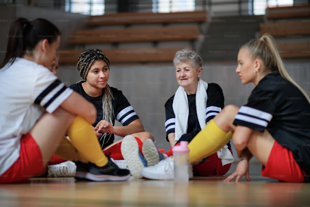 Group of young and old women, sports team players in gym sitting and talking after match.