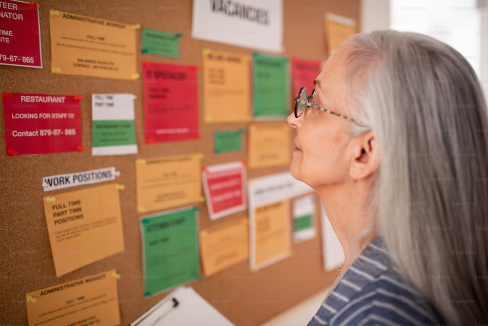 A job center employee with file form standing in front of employment noticeboard.