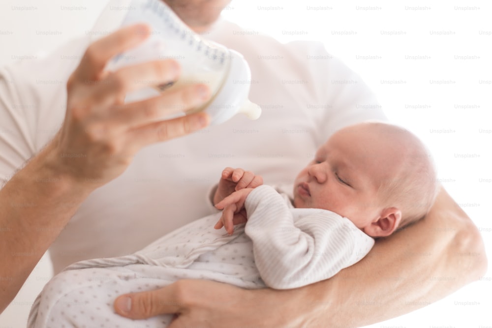 A father holding and feeding his newborn son with milk bottle at home.