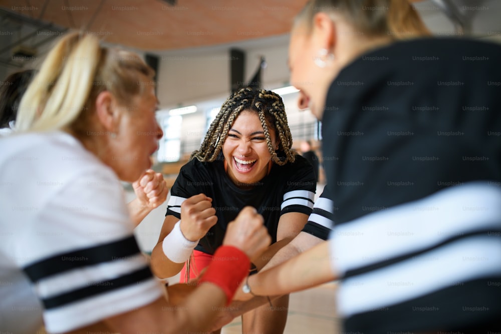 A group of young and old women in gym stacking hands together, sport team players.