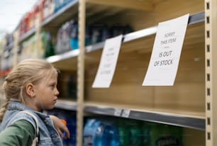 Una niña pequeña de compras y buscando vaciar los estantes en una tienda de comestibles