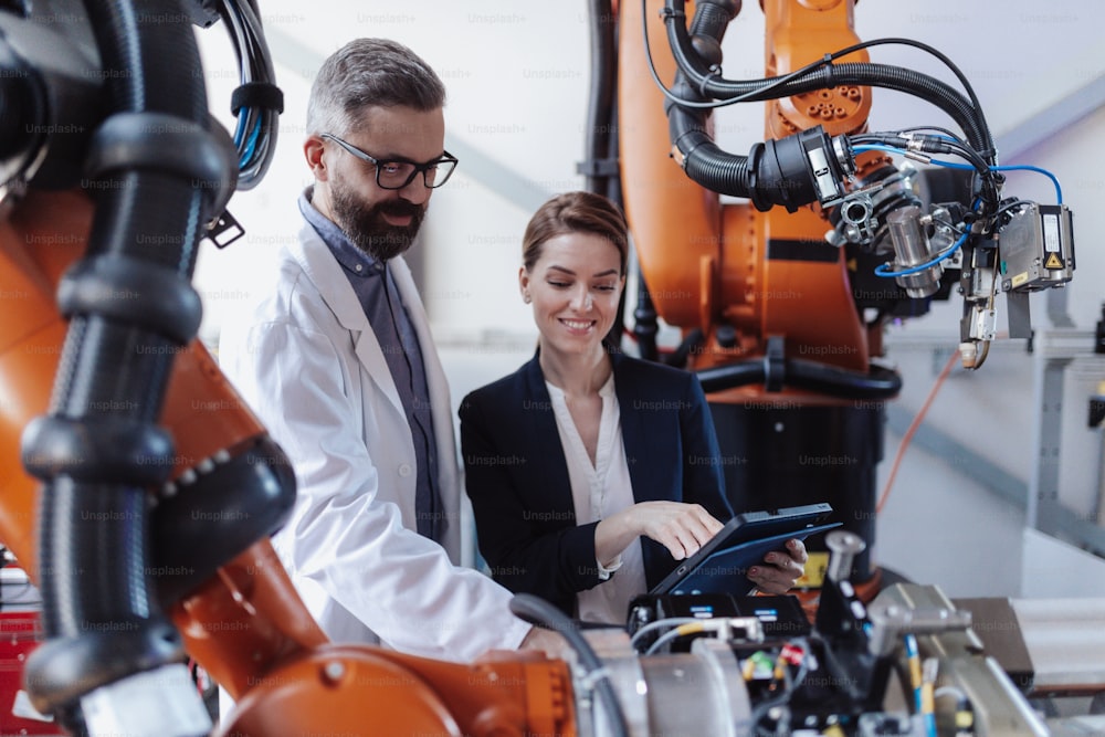 Robotics engineers with a tablet dicussing and desinging modern robotic arm in factory.