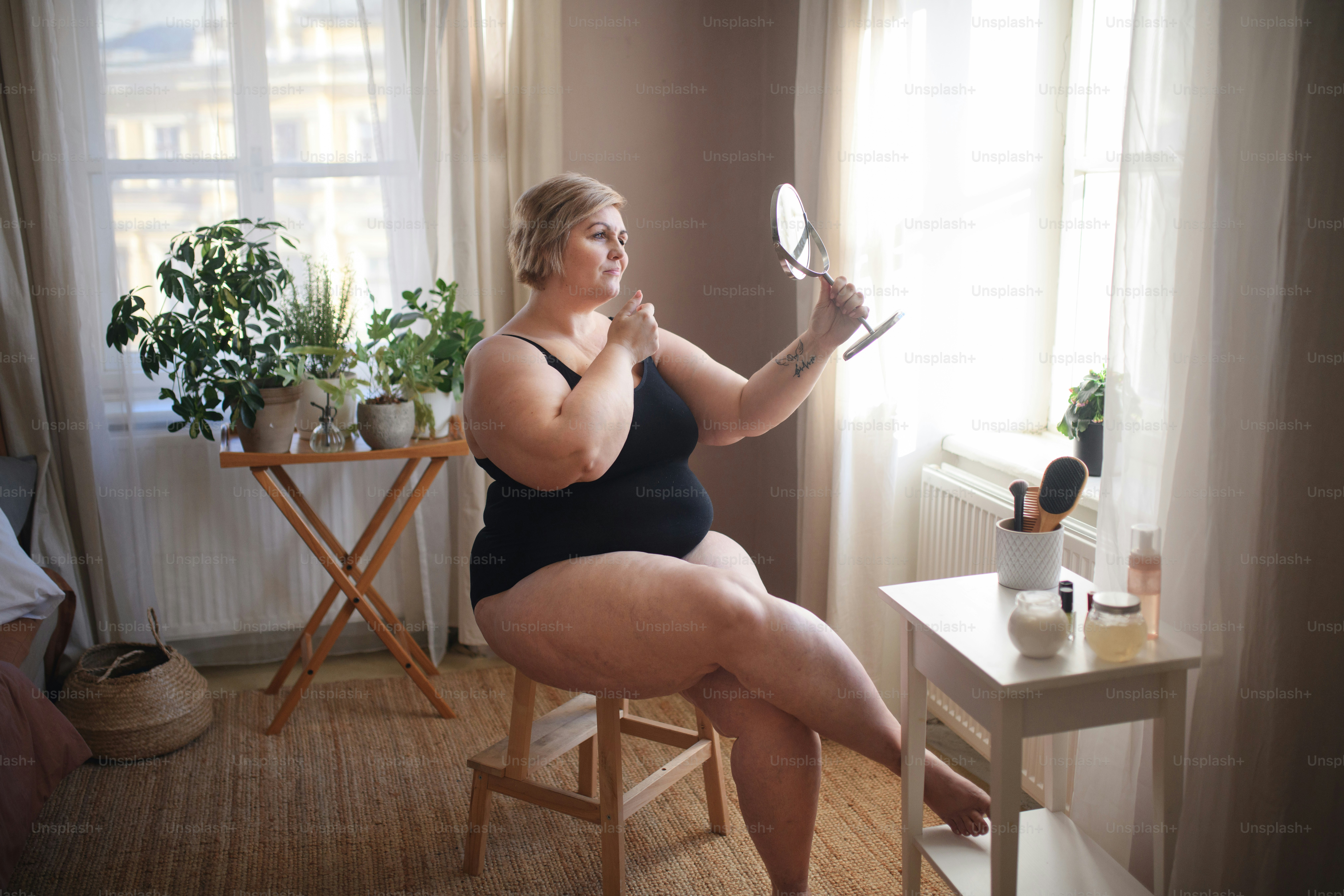 A fat woman sitting and looking at mirror at home, selfcare concept.