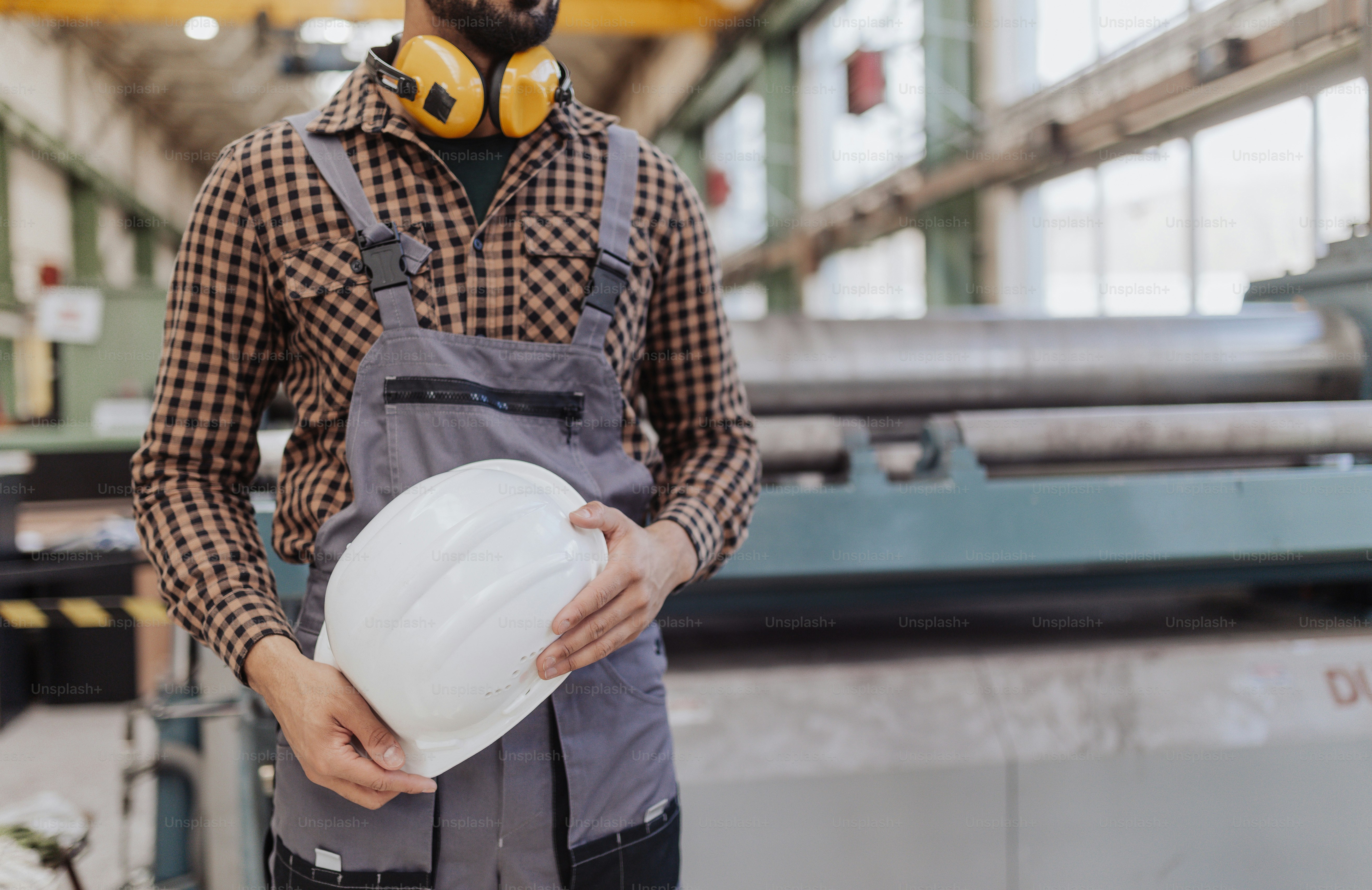 Una parte centrale dell'operaio dell'industria pesante con le cuffie di sicurezza e l'elmetto in fabbrica industriale