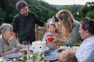 A multi generation family celebratiing birthday of little girl and having garden party outside on patio.