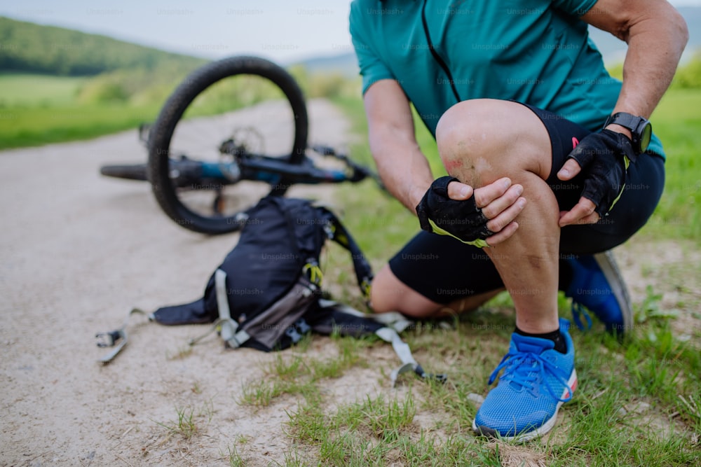 Um homem idoso ativo em roupas esportivas caiu de bicicleta no chão e machucou o joelho, no parque no verão.