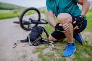 Un hombre mayor activo con ropa deportiva se cayó de la bicicleta al suelo y se lastimó la rodilla, en un parque en verano.