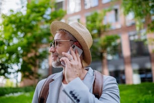 A confident man wearing straw hat and backpack talking on phone, businessman in casual clothes in summer on the way to work.