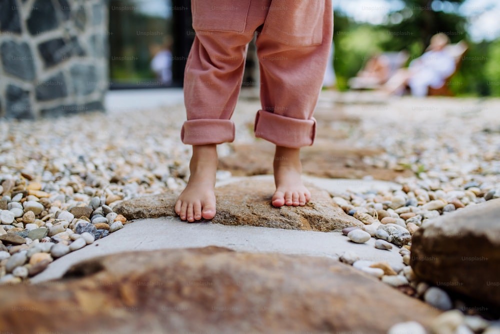 Primo piano di bambine gambe a piedi nudi, primi passi nel cortile durante una giornata estiva.